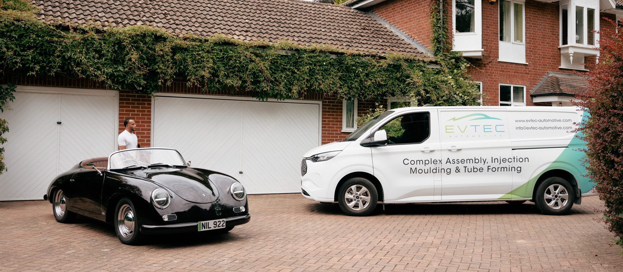A black classic car and a liveried Evtec service van parked side by side on a driveway