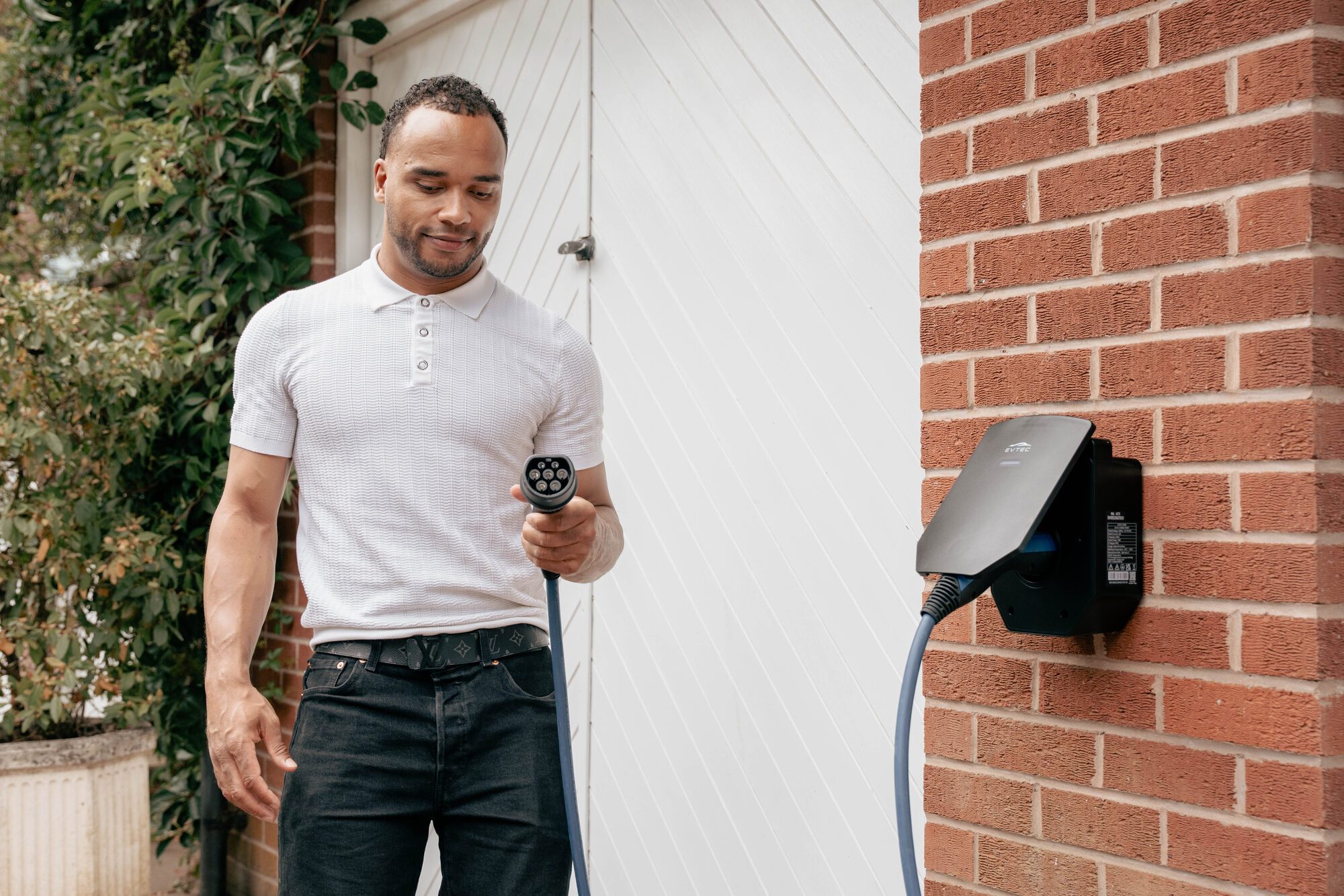 A man holding a charging connector beside a wall-mounted home charge point